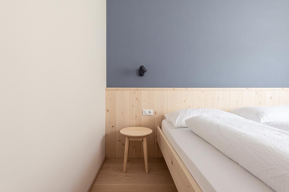 Schlafzimmer-Detail mit Holzkopfteil, blauer Akzentwand und Wandleuchte in Ferienwohnung Lana