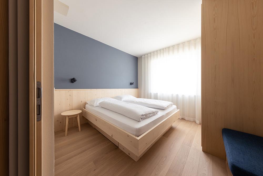 Helles Schlafzimmer mit Holzbett und blauer Akzentwand in Ferienwohnung Lana